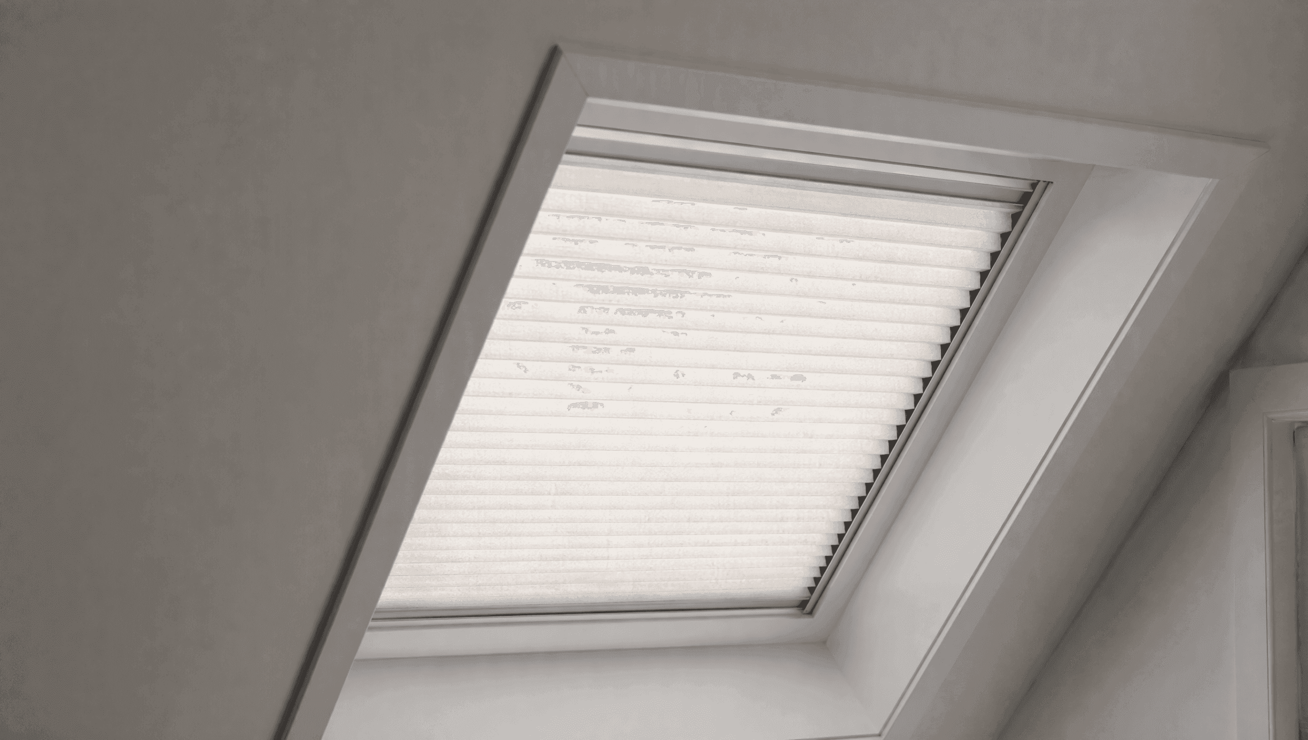 Motorized cellular skylight shade held flat in side channels inside an angled roof window