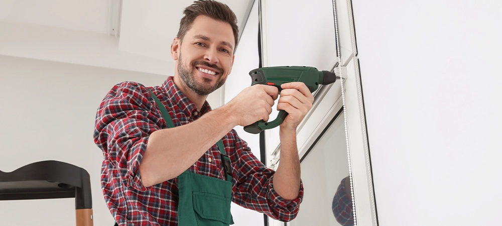 Worker in uniform installing roller window blind indoors