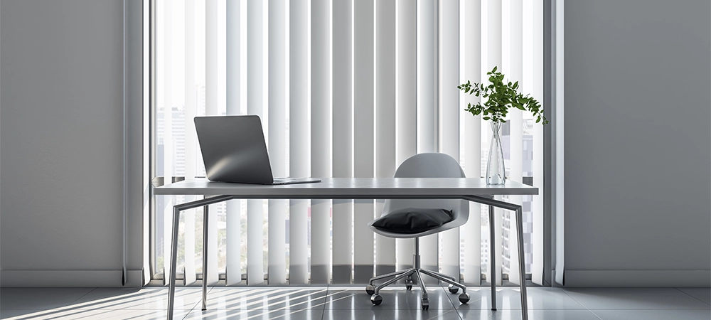 Stylish workplace in minimalistic office room with light table and chair, modern laptop, blinds on windows and sunlight on glossy floor. 3D rendering