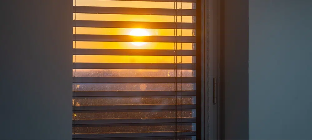 sunset seen trough automated external blinds in a skyscraper office building. Sun seen through a window with external venetian blinds