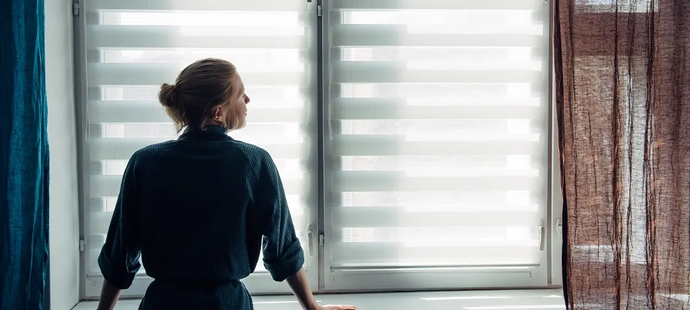 woman-in-gown-stands-near-window-with-zebra-blinds