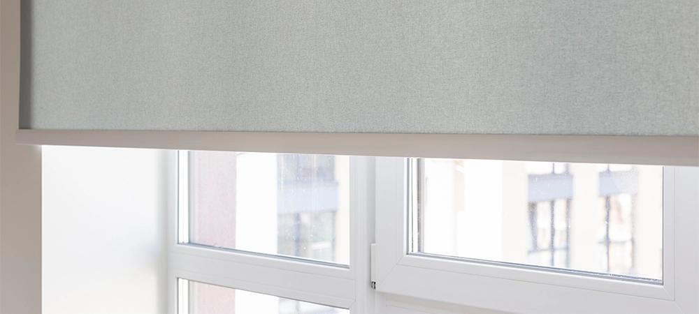 Details of gray fabric roller blinds. Automatic curtain close-up on the window. Selective focus. Motorized shades. City outside the window.