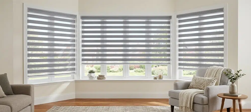 A full interior view of a bright living room featuring a large three-panel bay window fitted with modern grey and white zebra blinds.