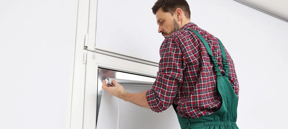 Worker in uniform installing roller window blind indoors