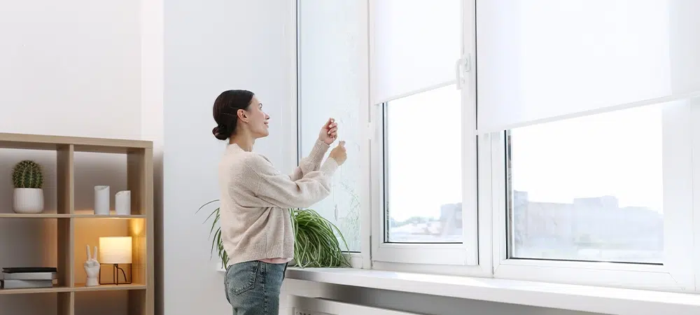 Woman opening roller blinds on window indoors