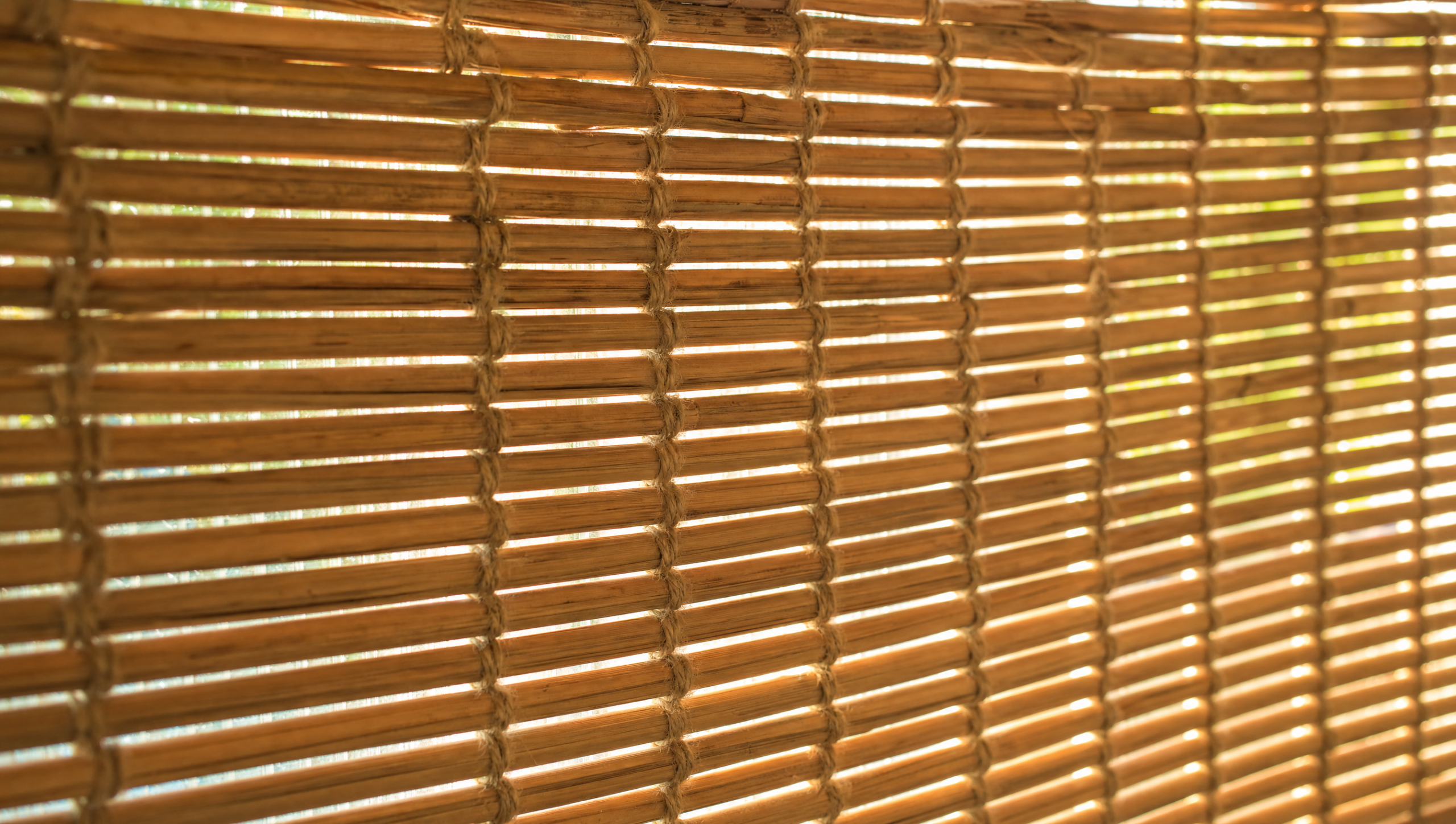 Close-up of a natural woven wood bamboo shade filtering warm daylight through the weave